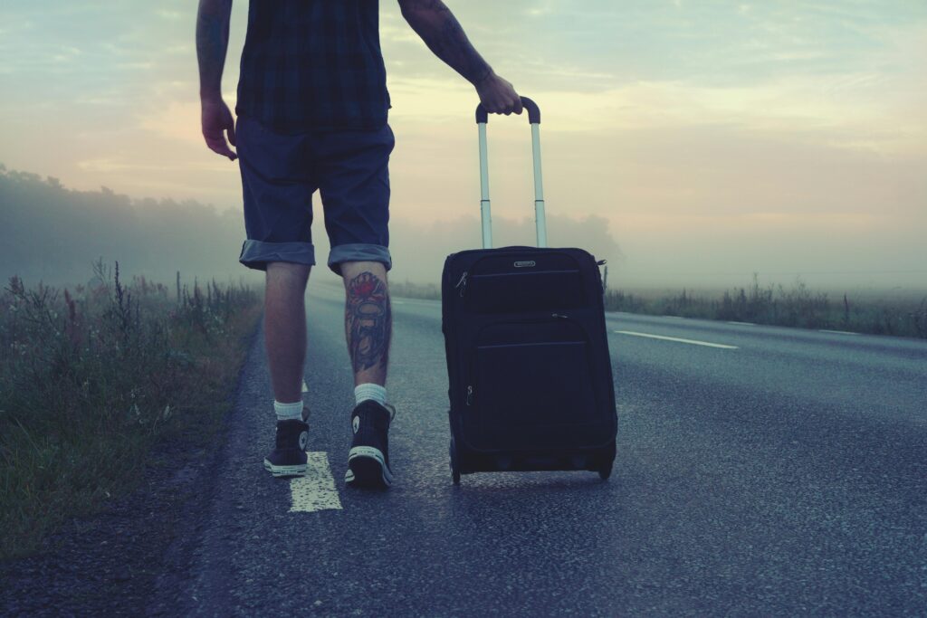 Viajante - Foto de Pixabay: https://www.pexels.com/pt-br/foto/homem-caminhando-na-estrada-segurando-bagagem-preta-durante-o-por-do-sol-160483/